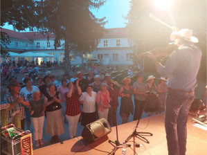 Ein Musiker spielt Geige auf einer Bühne vor einem Publikum im Freien bei Abenddämmerung.